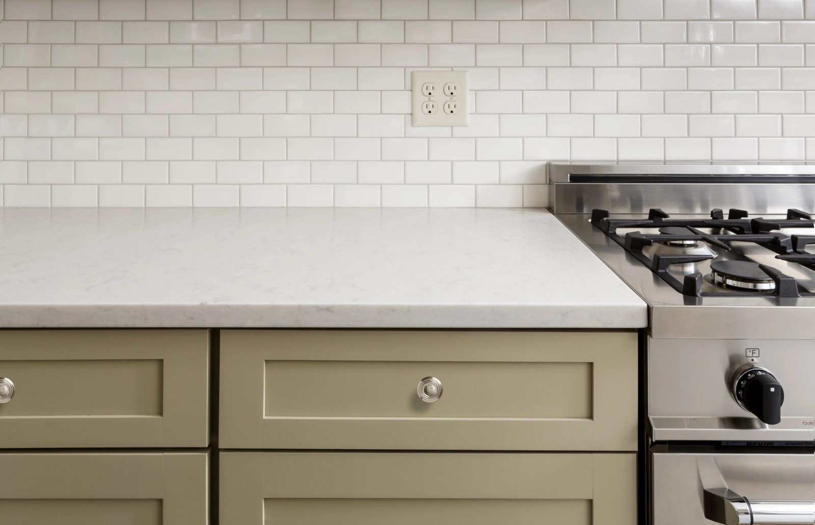White quartz countertop with a subway tile backsplash beside a stainless gas range